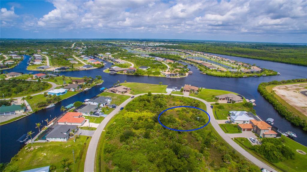 An aerial view shows a vacant, vegetated residential lot circled in blue within a waterfront neighborhood — 15505 MARGO CIRCLE, PORT CHARLOTTE, FL