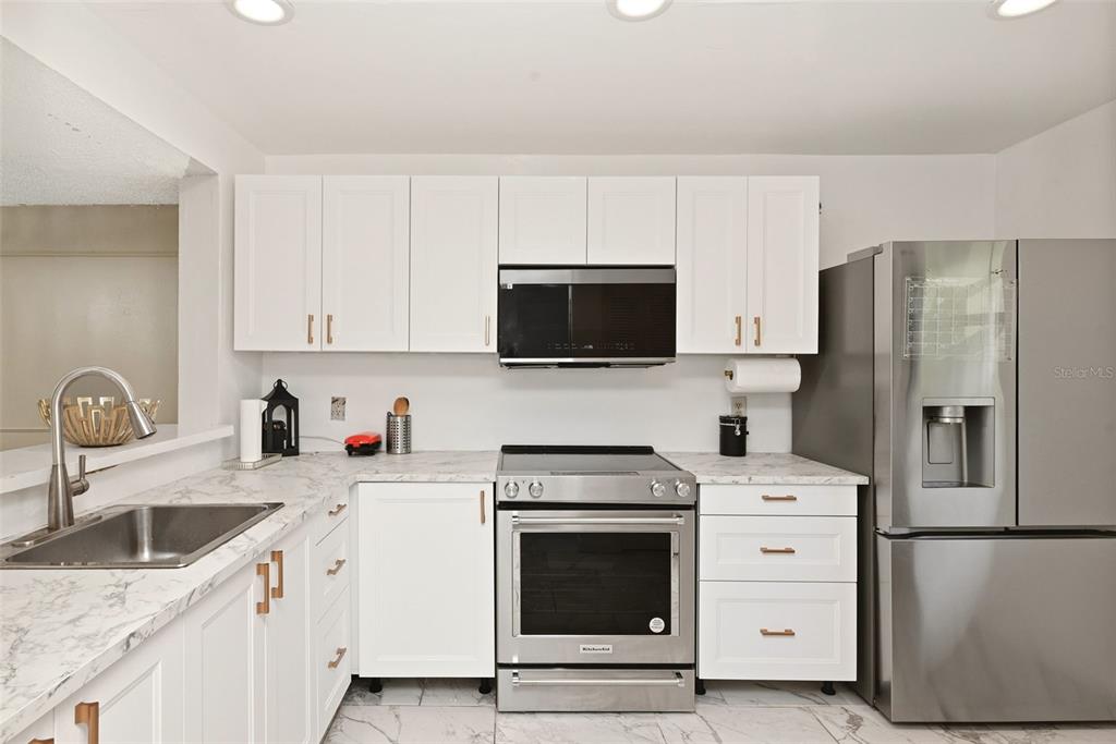 A kitchen features white cabinets, stainless steel appliances, and marble-patterned countertops — 2107 HONOUR ROAD UNIT 2107, ORLANDO, FL