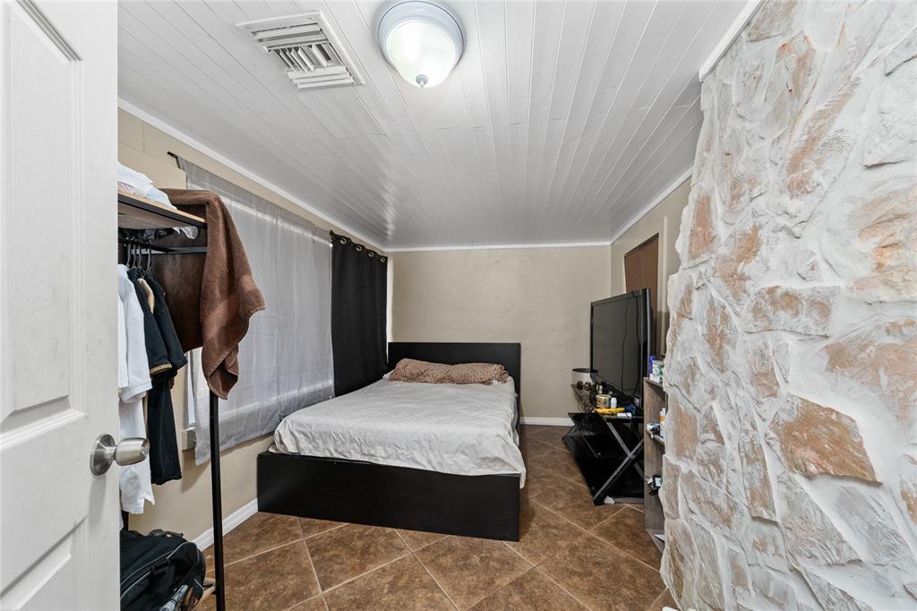A bedroom features a bed, a stone accent wall, and tiled flooring — 518 TOHOPEKALIGA AVENUE, KISSIMMEE, FL