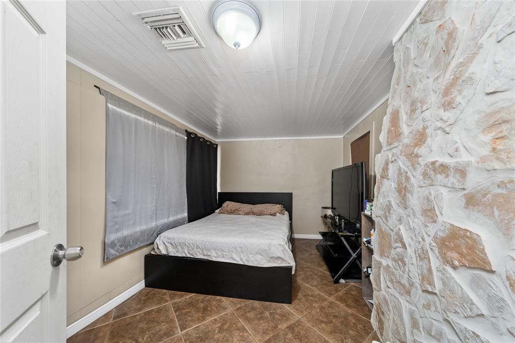 A bedroom features a bed, a television on a stand, and a stone accent wall — 518 TOHOPEKALIGA AVENUE, KISSIMMEE, FL
