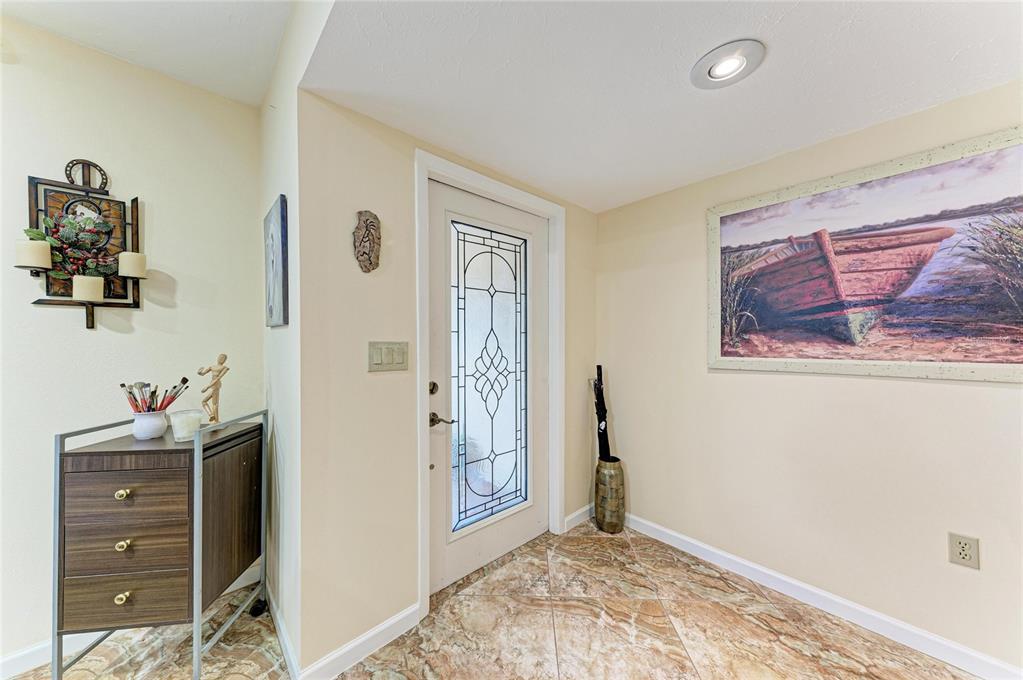 An entryway features a glass-paneled front door, tile flooring, a wooden cabinet, and wall art — 4533 KIPLING CIRCLE, SARASOTA, FL
