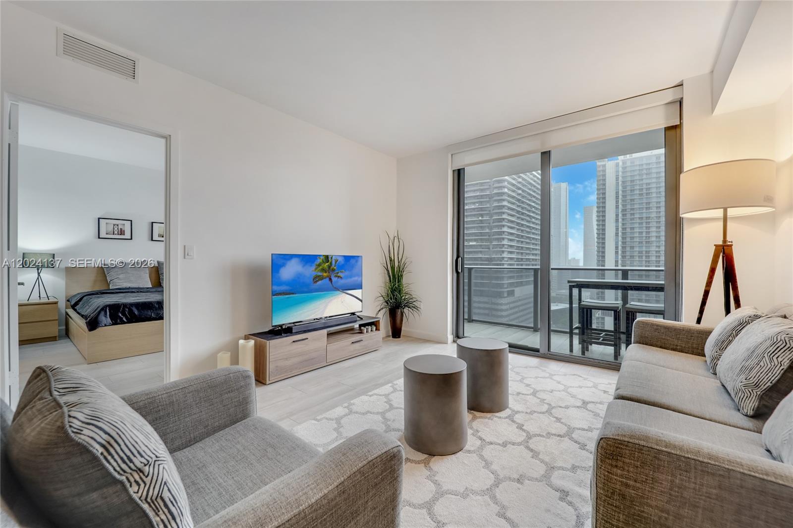A living room with a gray sofa, two cylindrical tables, and a balcony overlooking skyscrapers — 45 SW 9 ST # 1905, Miami FL 33130, MIAMI, FL