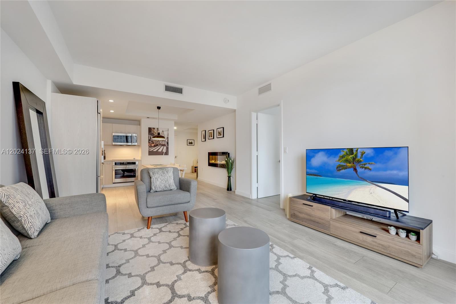 A living room with light wood floors, a grey sofa, and a television on a console — 45 SW 9 ST # 1905, Miami FL 33130, MIAMI, FL