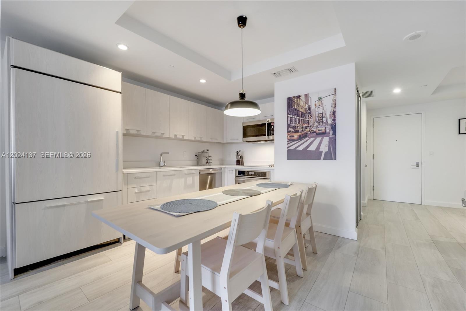 A modern kitchen features light wood cabinetry, a dining table, and a New York-themed print — 45 SW 9 ST # 1905, Miami FL 33130, MIAMI, FL