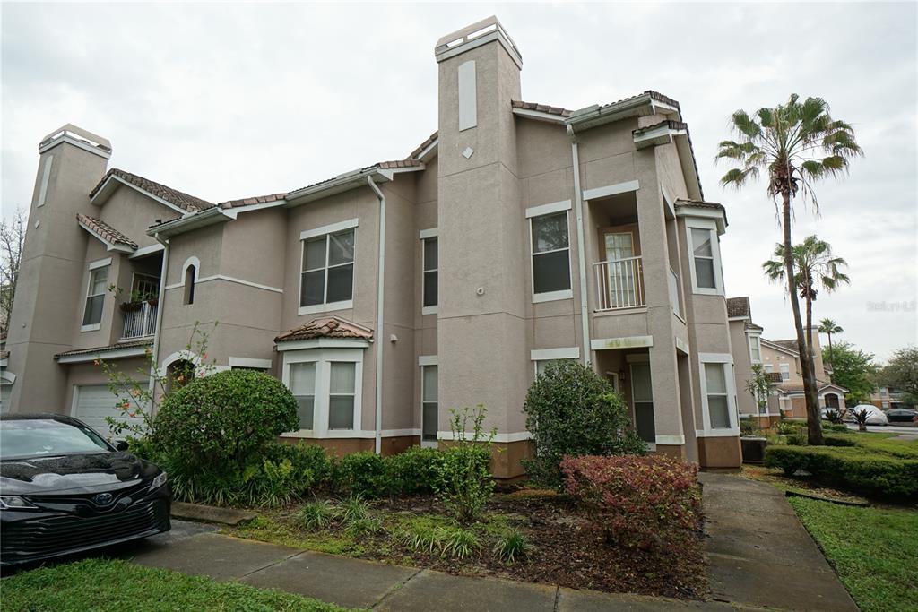 A two-story tan stucco townhouse with a chimney, a balcony, and a parked car — 18004 VILLA CREEK DRIVE, TAMPA, FL