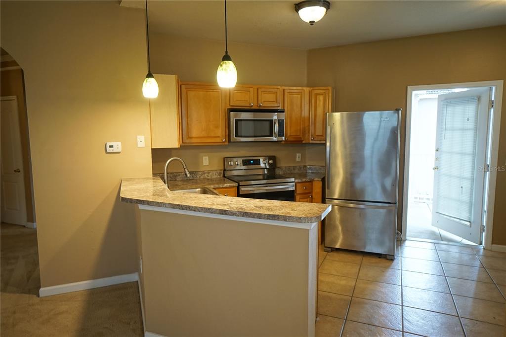 A kitchen features wood cabinets, stainless steel appliances, a breakfast bar, and tile flooring — 18004 VILLA CREEK DRIVE, TAMPA, FL