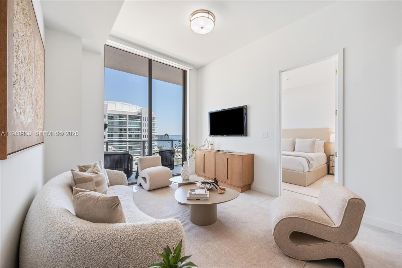 A modern living room features a curved sofa, two sculptural chairs, and a balcony view — 2655 S Bayshore Dr # 1608, Miami FL 33133, MIAMI, FL