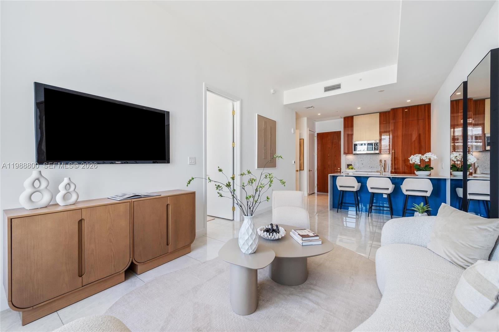 A modern living room features a television, wooden console, coffee tables, and an open kitchen — 2655 S Bayshore Dr # 1608, Miami FL 33133, MIAMI, FL