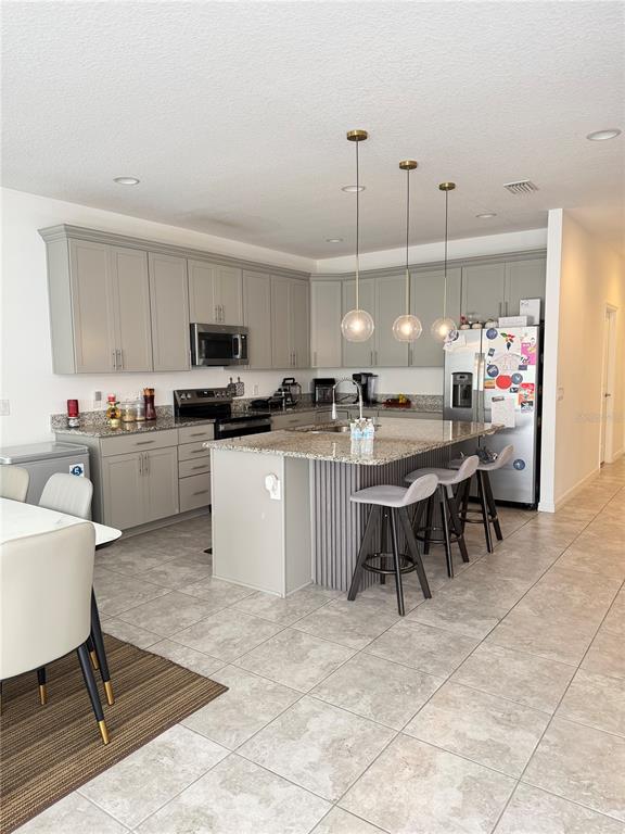 A kitchen features gray cabinetry, granite countertops, a center island with bar stools, and pendant lighting — 11102 HANLON TERRACE ALLEY, WINTER GARDEN, FL