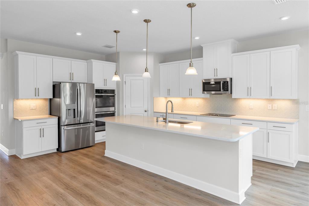 A bright, open-concept kitchen and dining area featuring white cabinetry, wood-look flooring, and pendant lighting — 1234 WHISPERING LANE, MINNEOLA, FL
