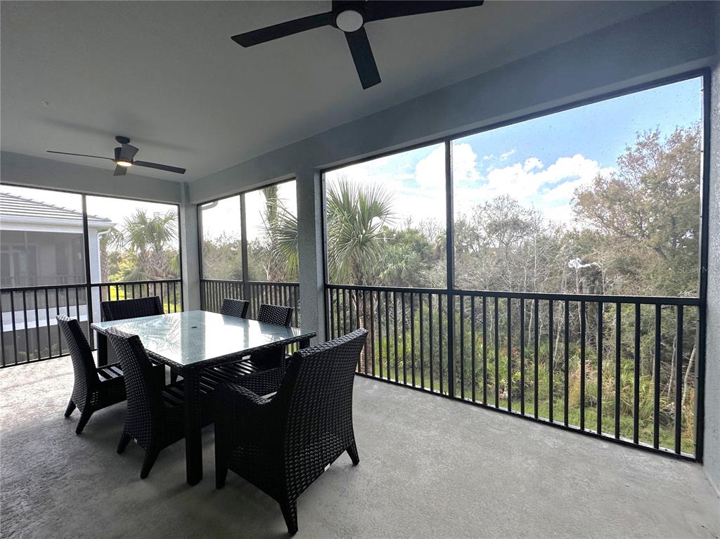 A screened-in patio features a dining set, ceiling fans, and a view of trees — 14185 POPPY FIELD LOOP UNIT 5421, PUNTA GORDA, FL