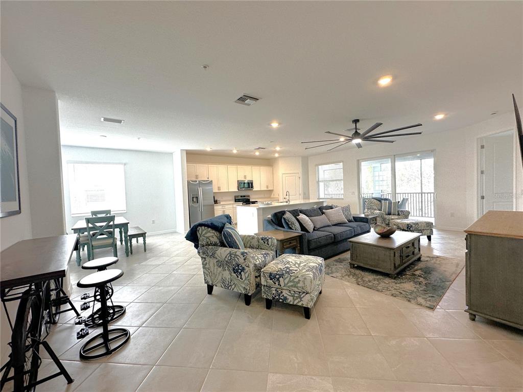 An open-concept living room and kitchen featuring tile flooring, a blue sofa, and patterned armchairs — 14185 POPPY FIELD LOOP UNIT 5421, PUNTA GORDA, FL