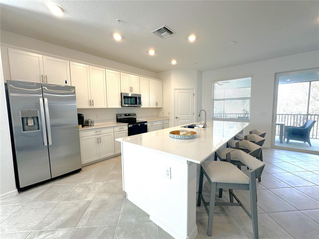 A modern kitchen features white cabinetry, stainless steel appliances, a large island, and tile flooring — 14185 POPPY FIELD LOOP UNIT 5421, PUNTA GORDA, FL