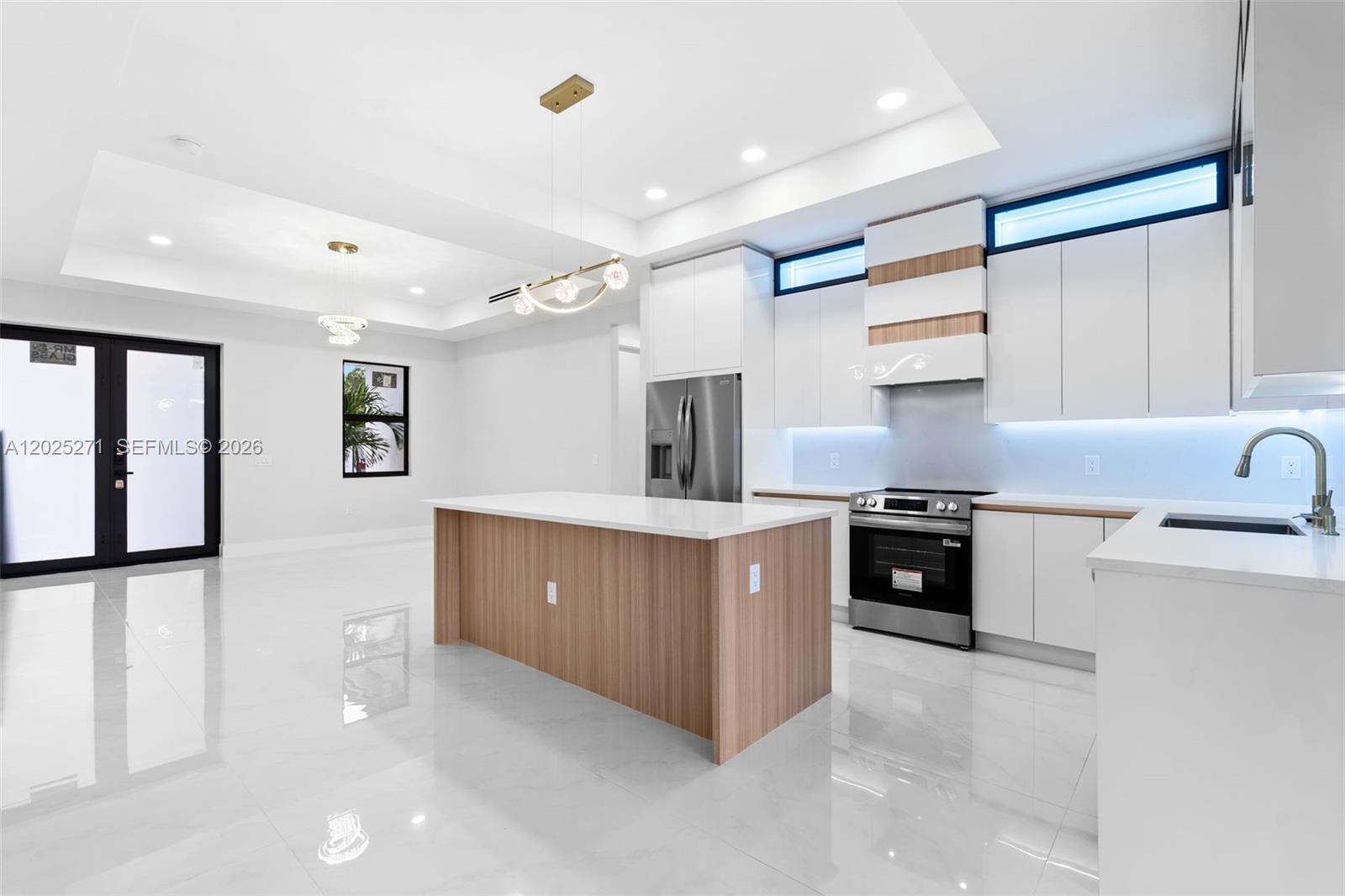 A modern kitchen features white cabinetry, a wood-toned island, and glossy tile flooring — LEHIGH ACRES, FL