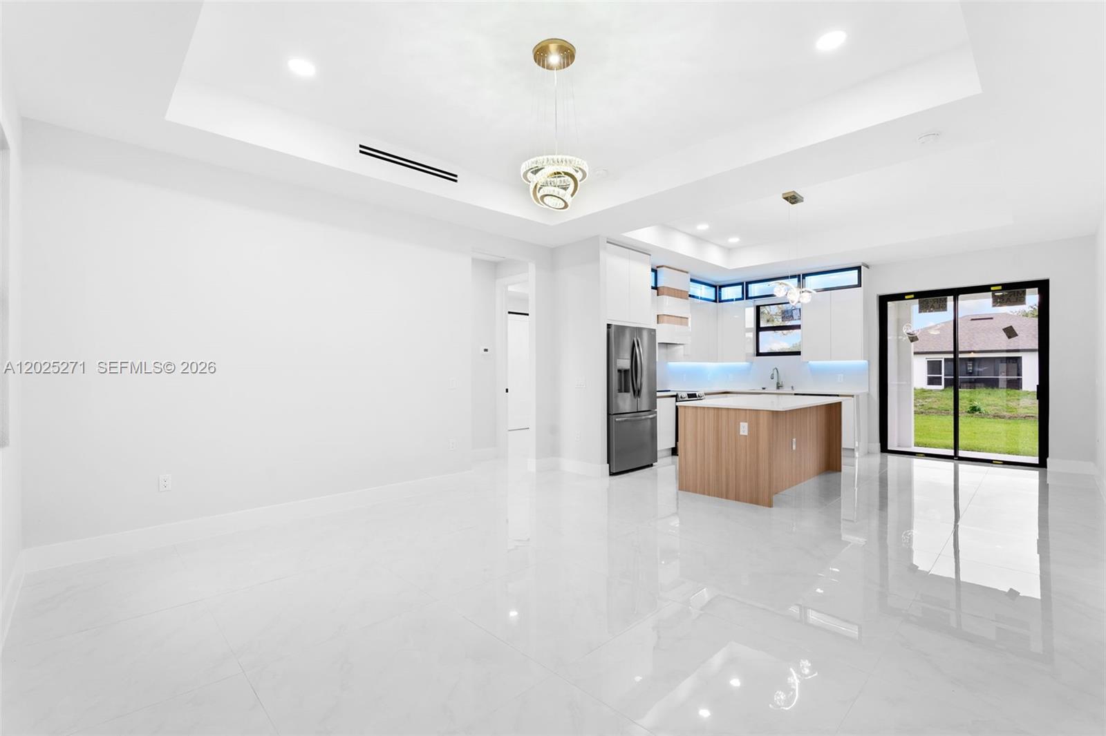 A modern open-concept kitchen and living area features white cabinetry, a wood-toned island, and tile — LEHIGH ACRES, FL