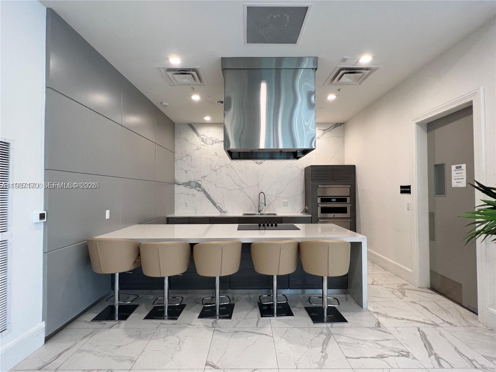 A modern kitchen features a marble backsplash, a large island with bar stools, and stainless appliances — 8167 NW 41st St # 308, Doral FL 33166, DORAL, FL