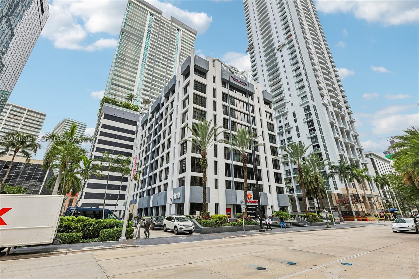 A low-rise office building stands between two tall residential towers on a city street — 1110 Brickell Ave # 512, Miami FL 33131, MIAMI, FL