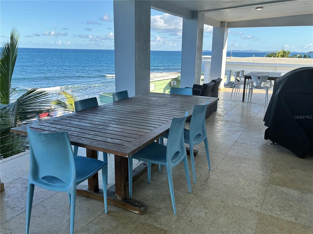 A large wooden dining table with blue chairs sits on a covered oceanfront patio — 365 NORTH SHORE POINTE, VIEQUES, PR