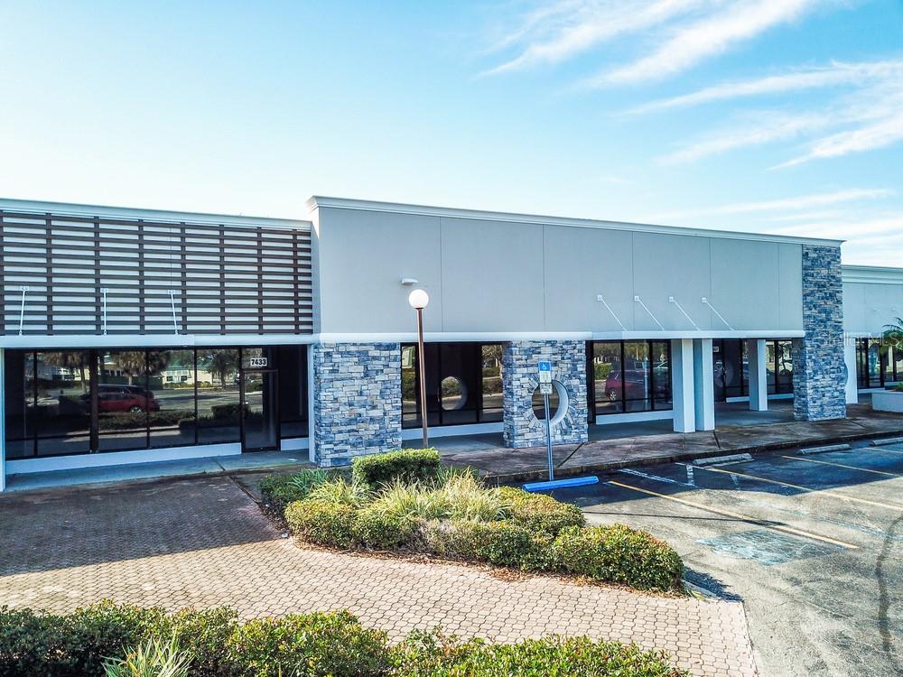 An exterior view of a commercial building with stone accents, glass storefronts, and parking spaces — 7421 MANATEE AVENUE W UNIT 7453, BRADENTON, FL