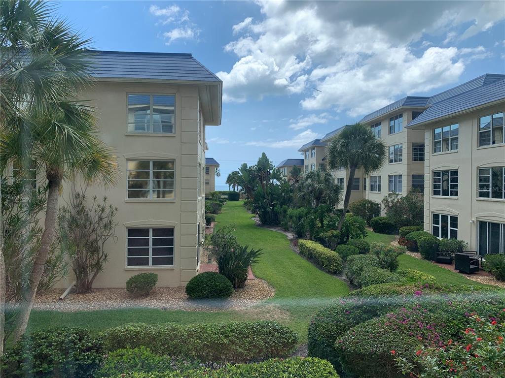 An exterior view of apartment buildings with a grassy courtyard leading toward the ocean — 3806 GULF OF MEXICO DRIVE UNIT C310, LONGBOAT KEY, FL
