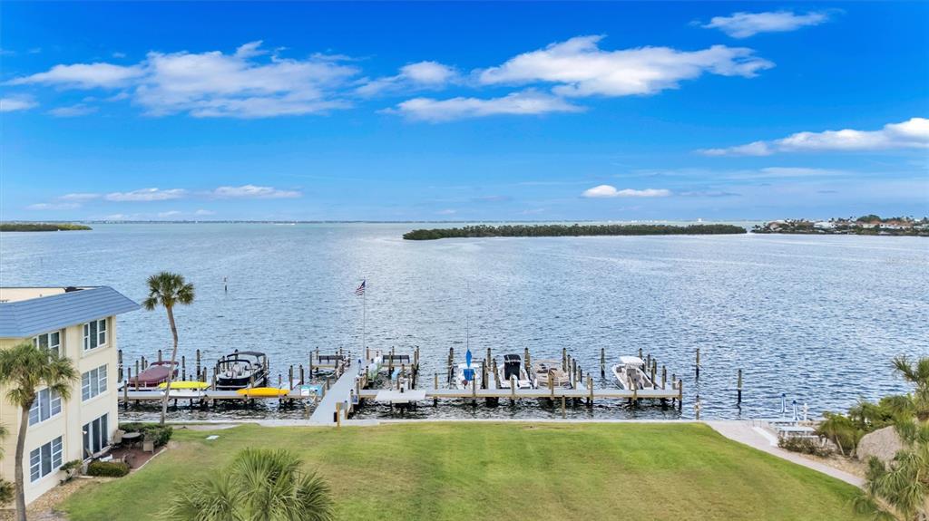 An aerial view of a waterfront property featuring a boat dock, lawn, and blue sky — 3806 GULF OF MEXICO DRIVE UNIT C310, LONGBOAT KEY, FL