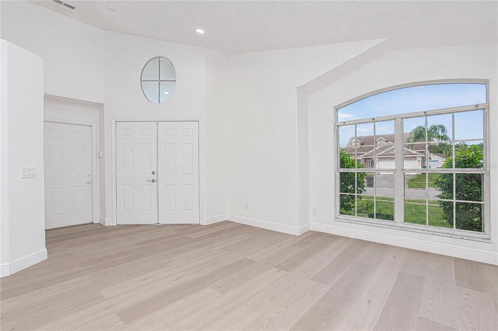 An empty room with light wood-look flooring, white walls, double entry doors, and a large window — 2039 SHANNON LAKES BOULEVARD, KISSIMMEE, FL