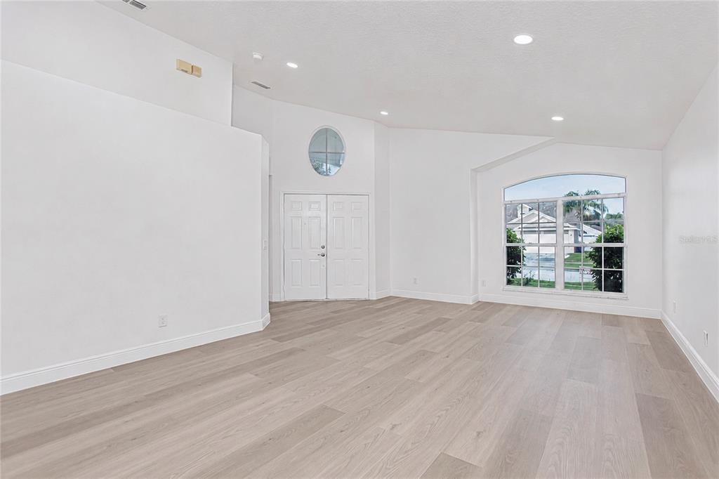 A bright, empty living room features light wood-look flooring, white walls, and a large arched window — 2039 SHANNON LAKES BOULEVARD, KISSIMMEE, FL