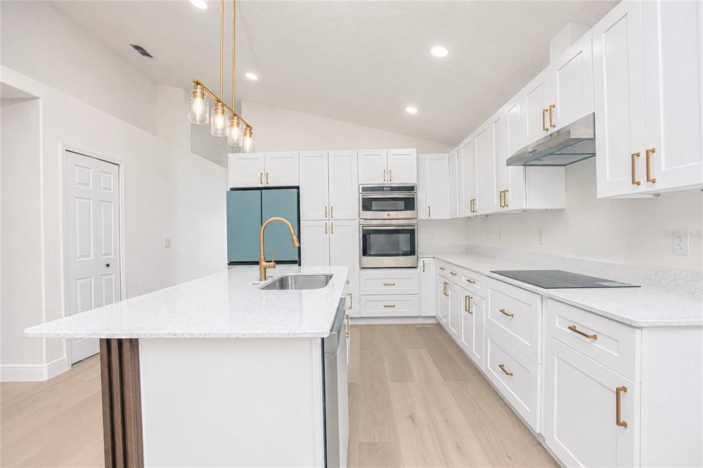 A modern white kitchen features a large island, stainless steel appliances, and light wood flooring — 2039 SHANNON LAKES BOULEVARD, KISSIMMEE, FL