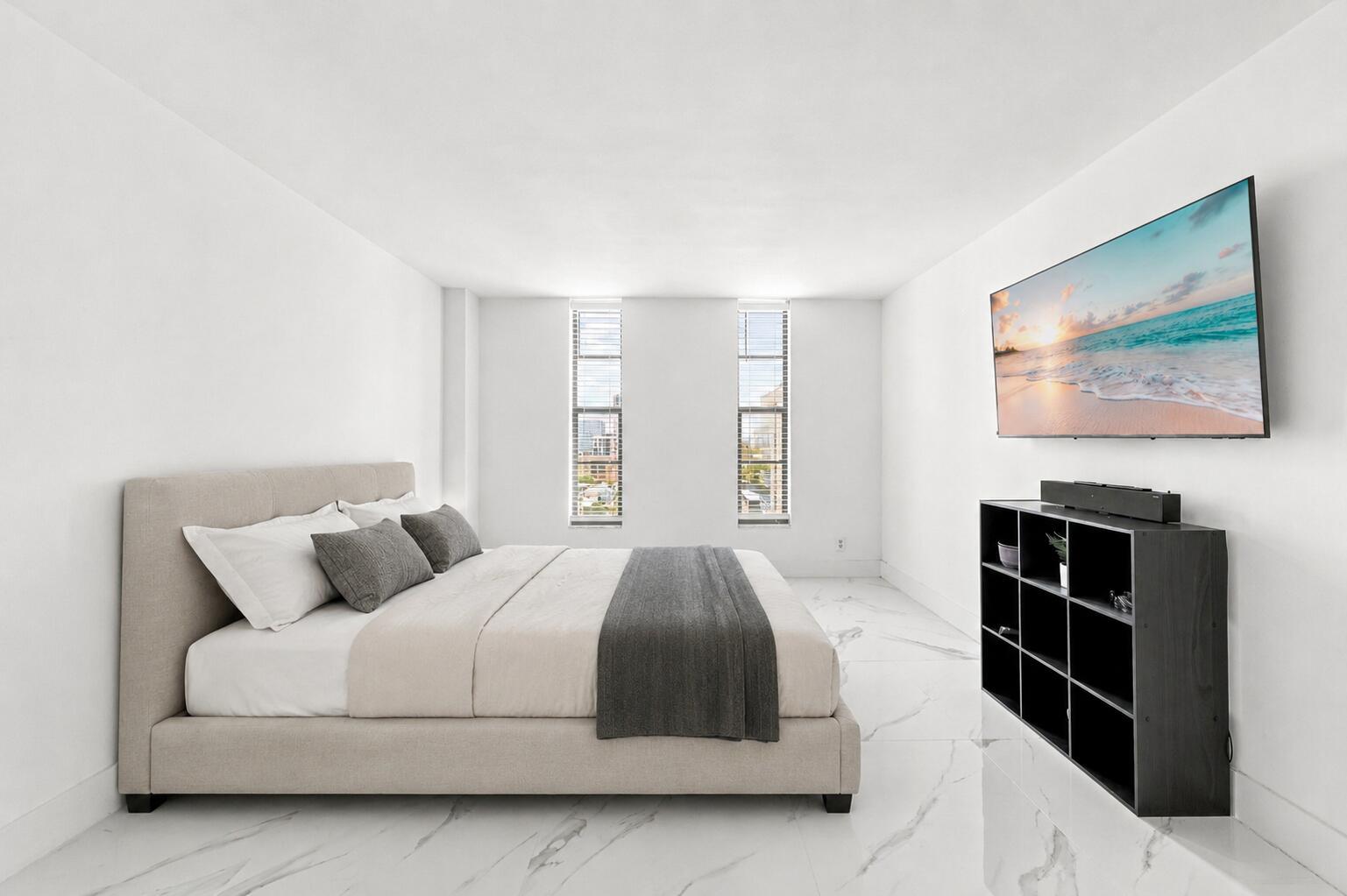 A bedroom features a beige upholstered bed, a black shelving unit, and white marble flooring — 1000 S Ocean Boulevard # 14o, Pompano Beach FL 33062, POMPANO BEACH, FL