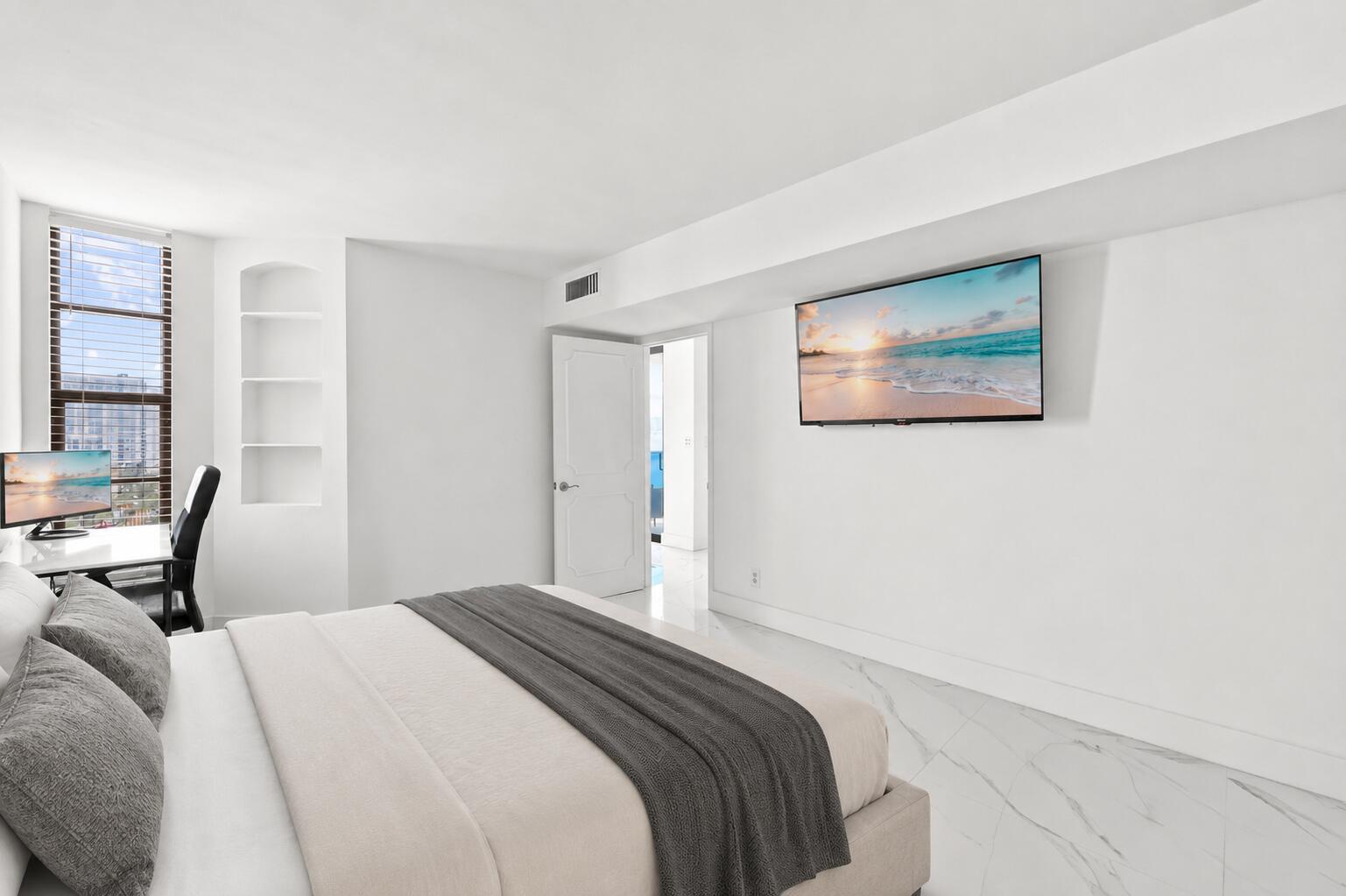 A bedroom features a bed, a wall-mounted television, a desk, and white marble flooring — 1000 S Ocean Boulevard # 14o, Pompano Beach FL 33062, POMPANO BEACH, FL