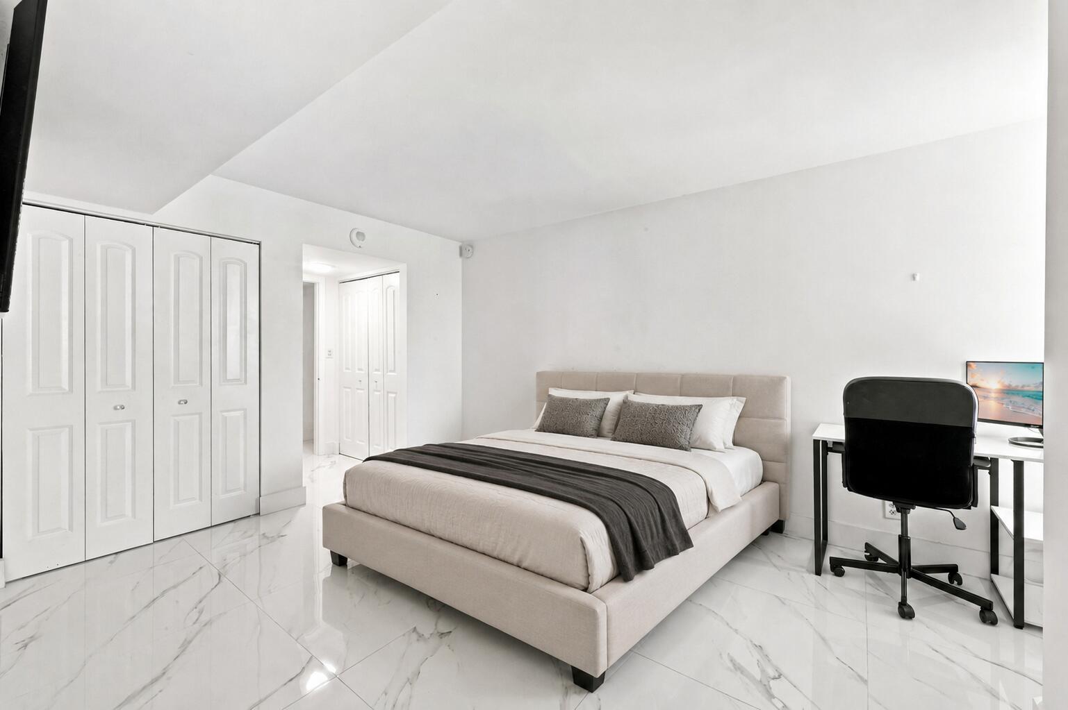 A bedroom features a bed, a desk with a chair, and white marble-style flooring — 1000 S Ocean Boulevard # 14o, Pompano Beach FL 33062, POMPANO BEACH, FL