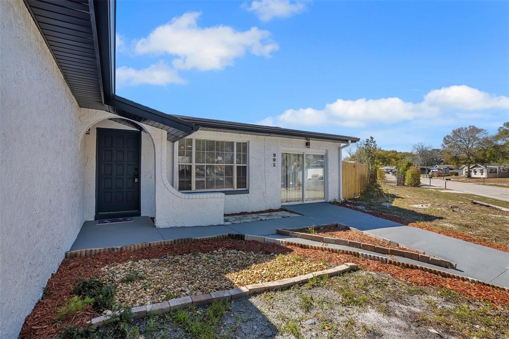 A white stucco house exterior features a dark front door, sliding glass doors, and landscaping — 905 SPRING CREEK DRIVE, OCOEE, FL