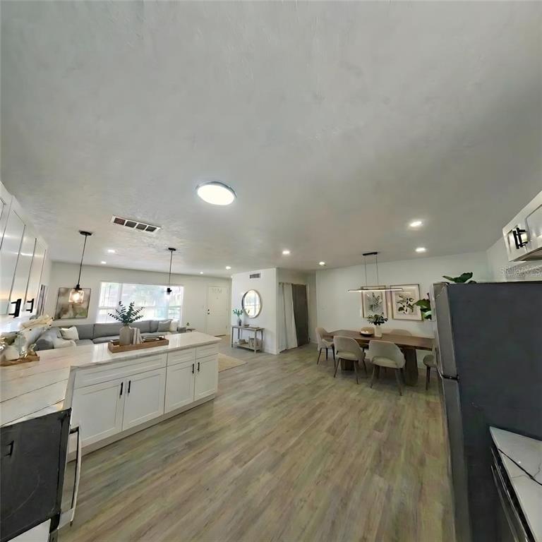An open-concept living and dining area features white cabinetry, wood-look flooring, and recessed lighting — 905 SPRING CREEK DRIVE, OCOEE, FL