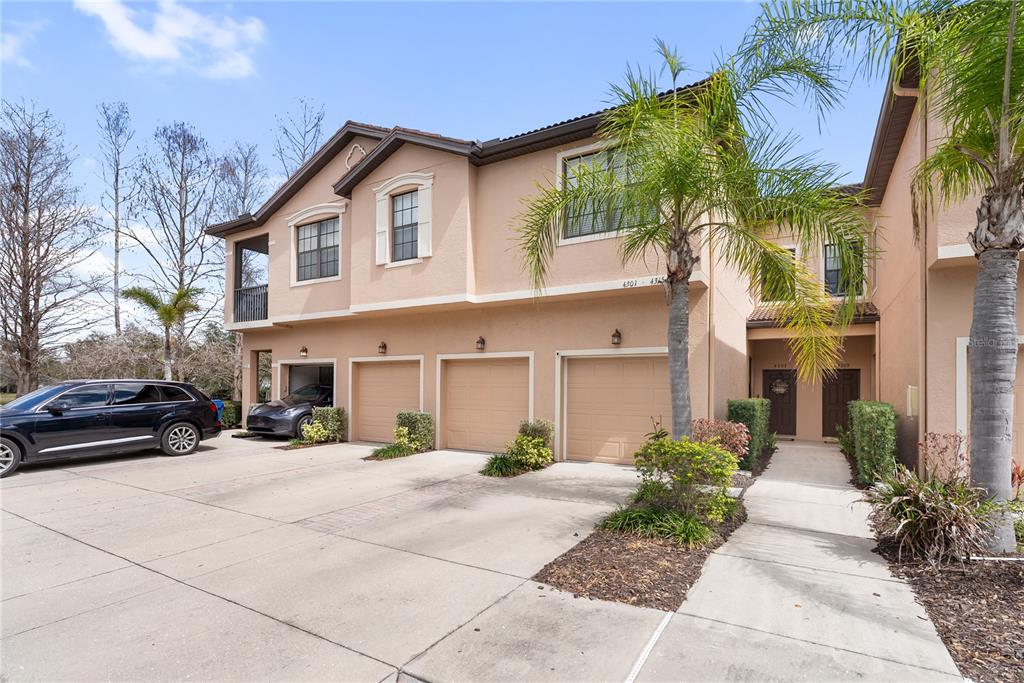 A multi-unit residential building with beige stucco, multiple garage doors, and a palm tree — 4307 VIA PIEDRA CIRCLE UNIT 6-102, SARASOTA, FL
