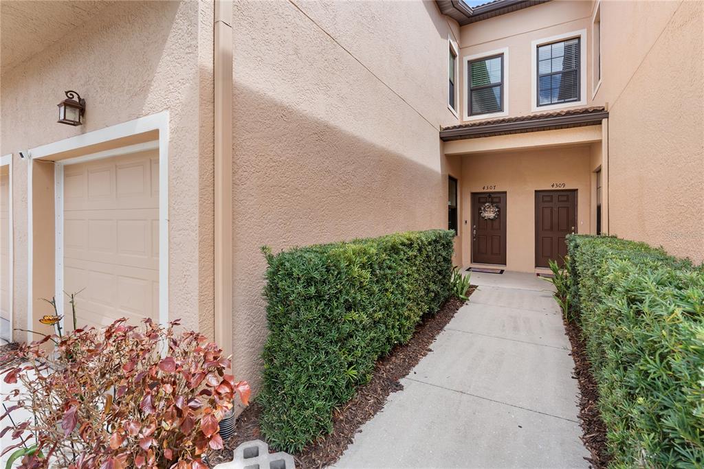 A concrete walkway leads to two brown front doors of a tan stucco townhouse — 4307 VIA PIEDRA CIRCLE UNIT 6-102, SARASOTA, FL