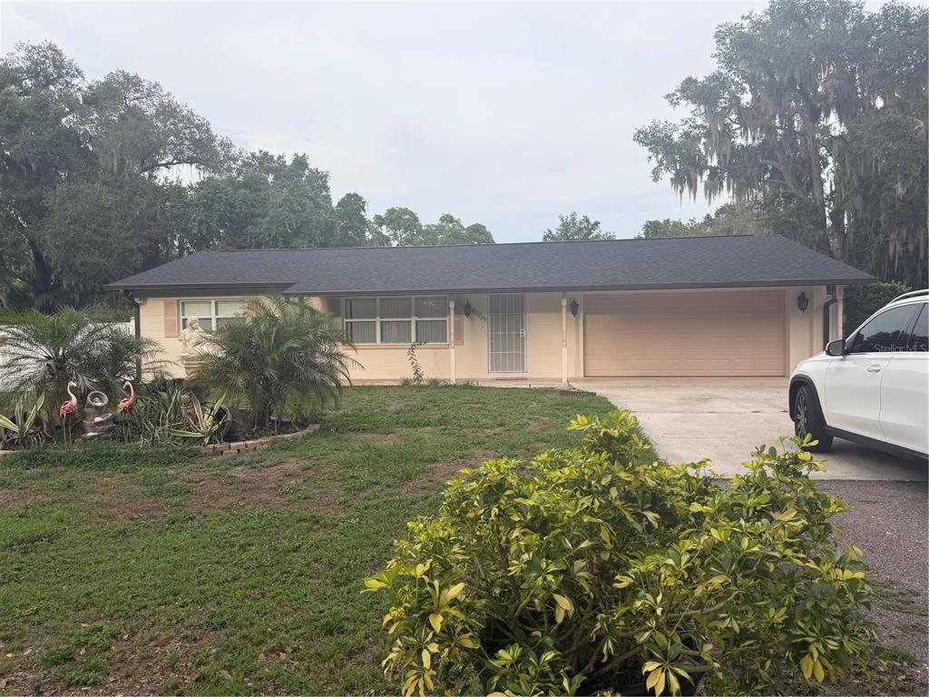 A single-story house with a tan exterior, dark roof, and attached garage sits on grass — 8009 PAULSON LANE, TAMPA, FL