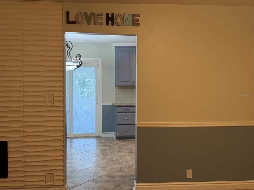 A view through a doorway shows a kitchen with blue cabinets and tile flooring — 8009 PAULSON LANE, TAMPA, FL