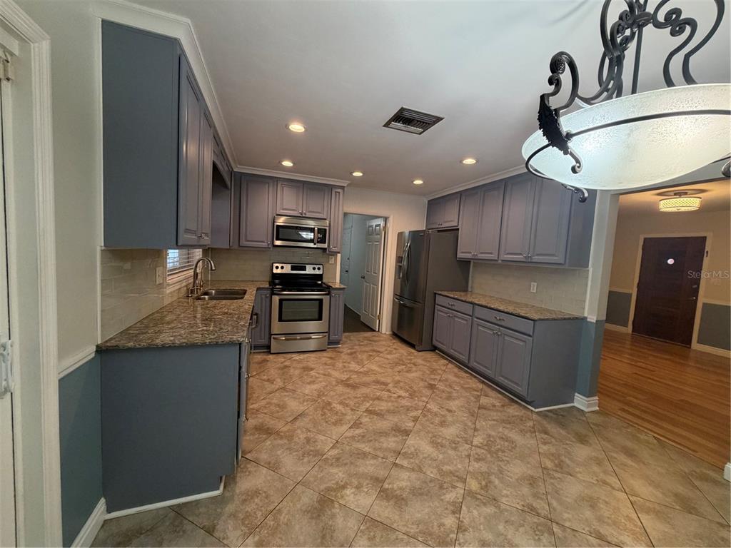 A kitchen features blue cabinets, granite countertops, stainless steel appliances, and tile flooring — 8009 PAULSON LANE, TAMPA, FL