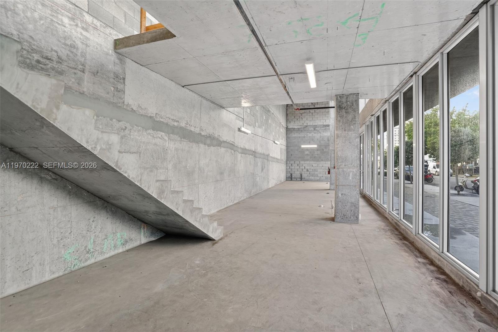 An unfinished industrial-style space features exposed concrete walls, a concrete staircase, and floor-to-ceiling windows — 1110 NW 1 ST, Miami FL 33128, MIAMI, FL