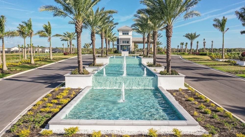 A tiered fountain sits between two roads leading toward a gated community entrance with palms — 10141 MILKY WAY CIRCLE, SARASOTA, FL