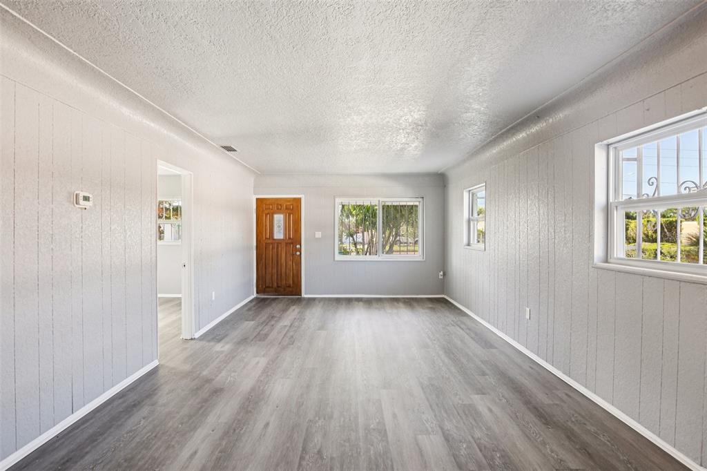 A living room with gray wood-look flooring, light gray paneled walls, and a wooden door — 1911 22ND AVENUE S, ST PETERSBURG, FL