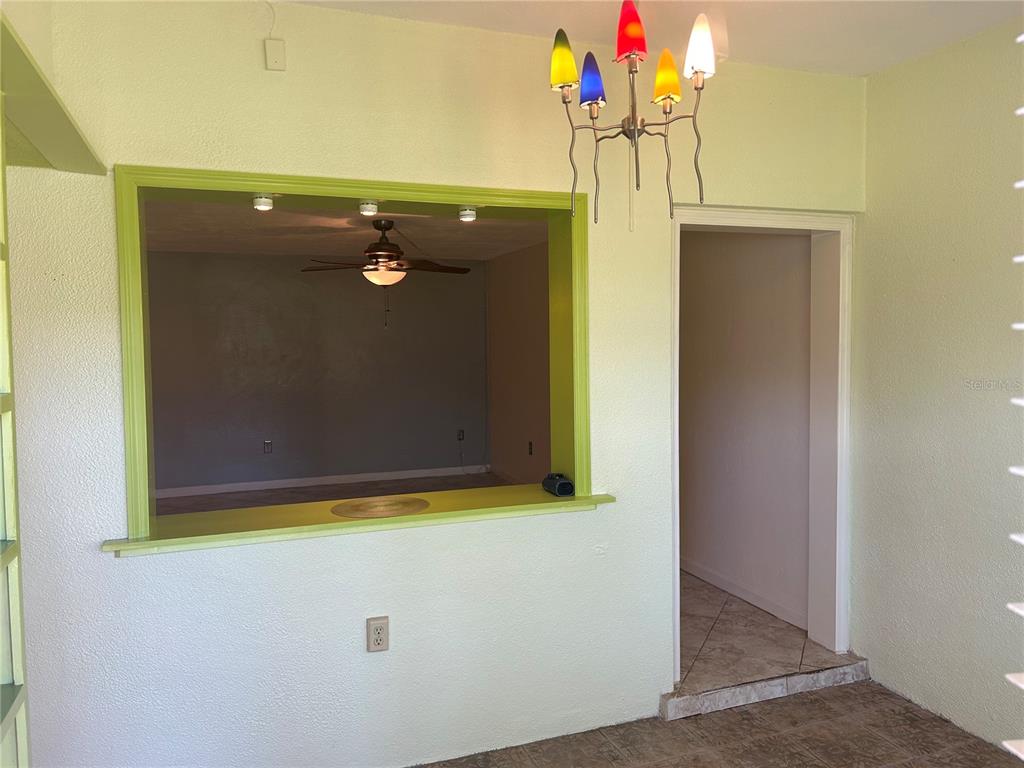 A dining area features a colorful multi-light chandelier and a pass-through window to another room — 445 32ND AVENUE N UNIT E109, ST PETERSBURG, FL
