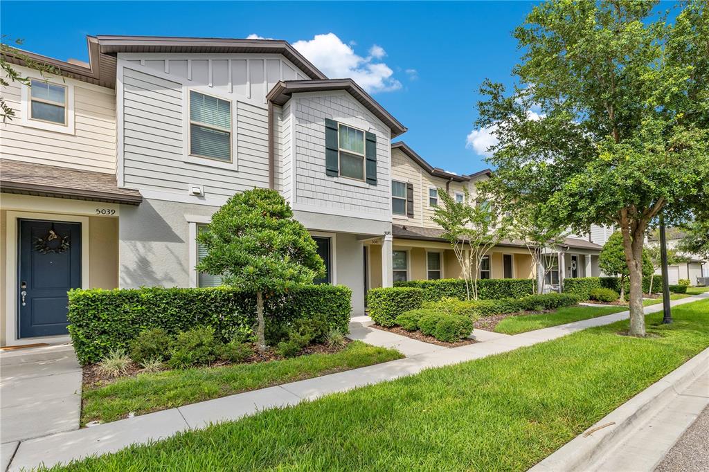 A two-story townhouse exterior with light-colored siding, a dark blue front door, and manicured hedges — 5041 CASPIAN STREET, ST CLOUD, FL