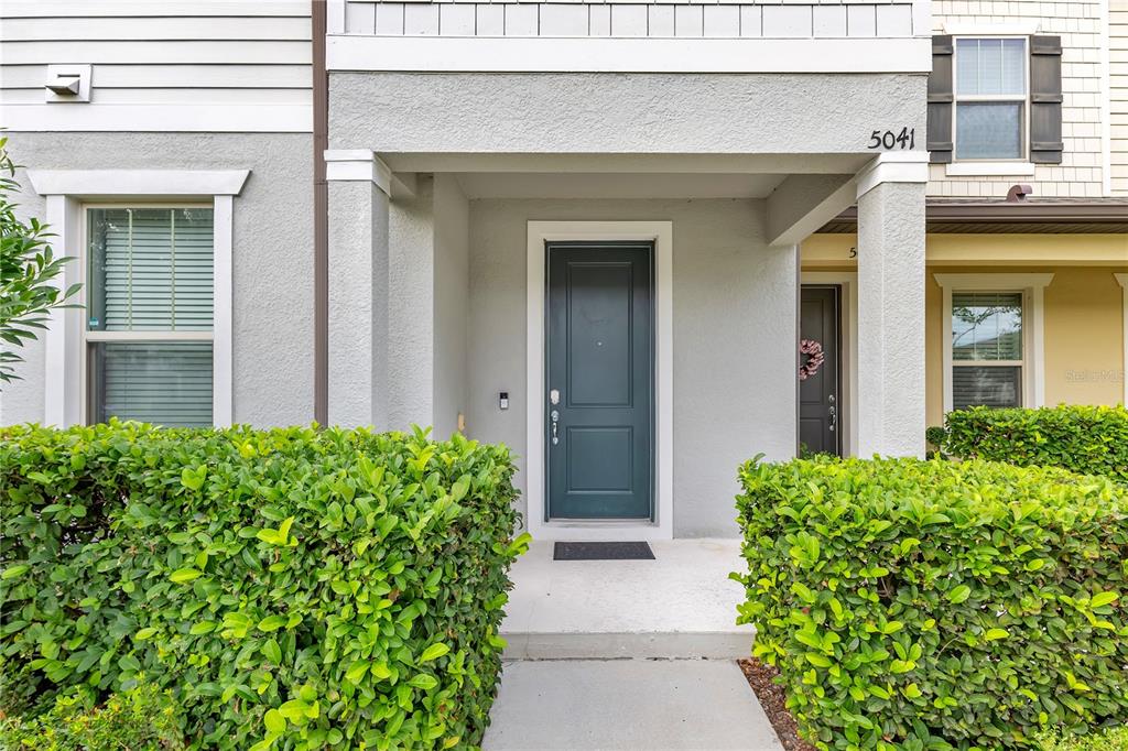 A front entrance with a dark door, a concrete porch, and manicured green hedges — 5041 CASPIAN STREET, ST CLOUD, FL