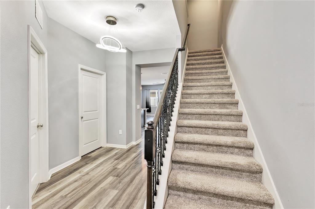 An entryway features wood-look flooring, a carpeted staircase with a metal railing, and light-colored walls — 5041 CASPIAN STREET, ST CLOUD, FL