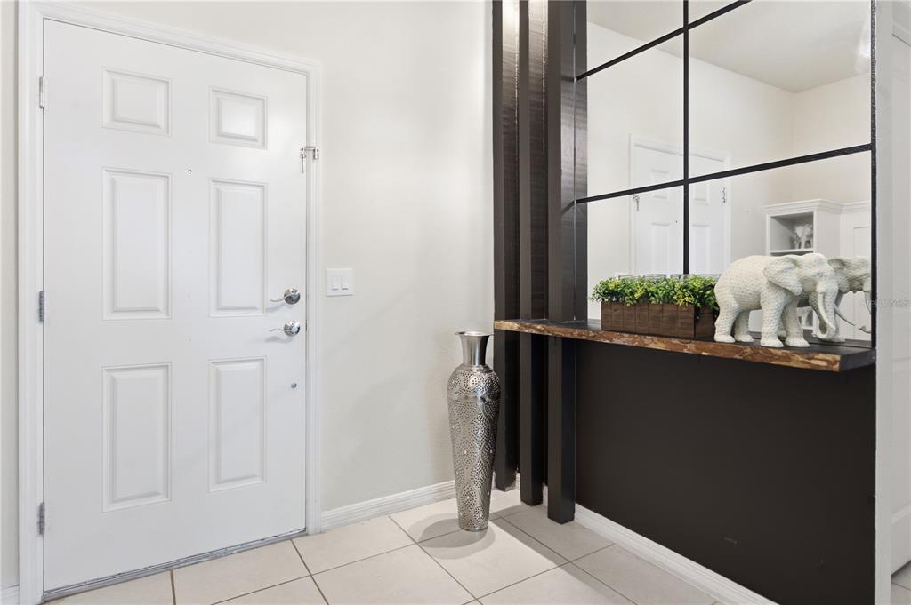 An entryway features a white door, tiled floor, a tall silver vase, and a mirror — 3954 LANA AVENUE, DAVENPORT, FL