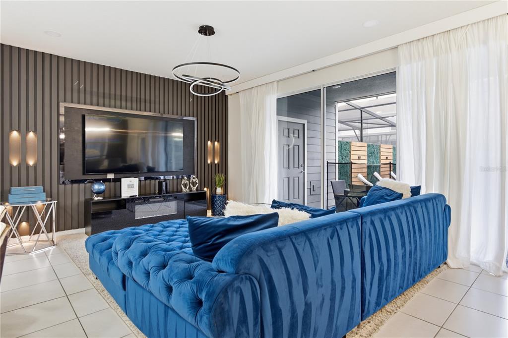 A living room features a blue tufted sofa, a wall-mounted television, and a sliding glass door — 3954 LANA AVENUE, DAVENPORT, FL
