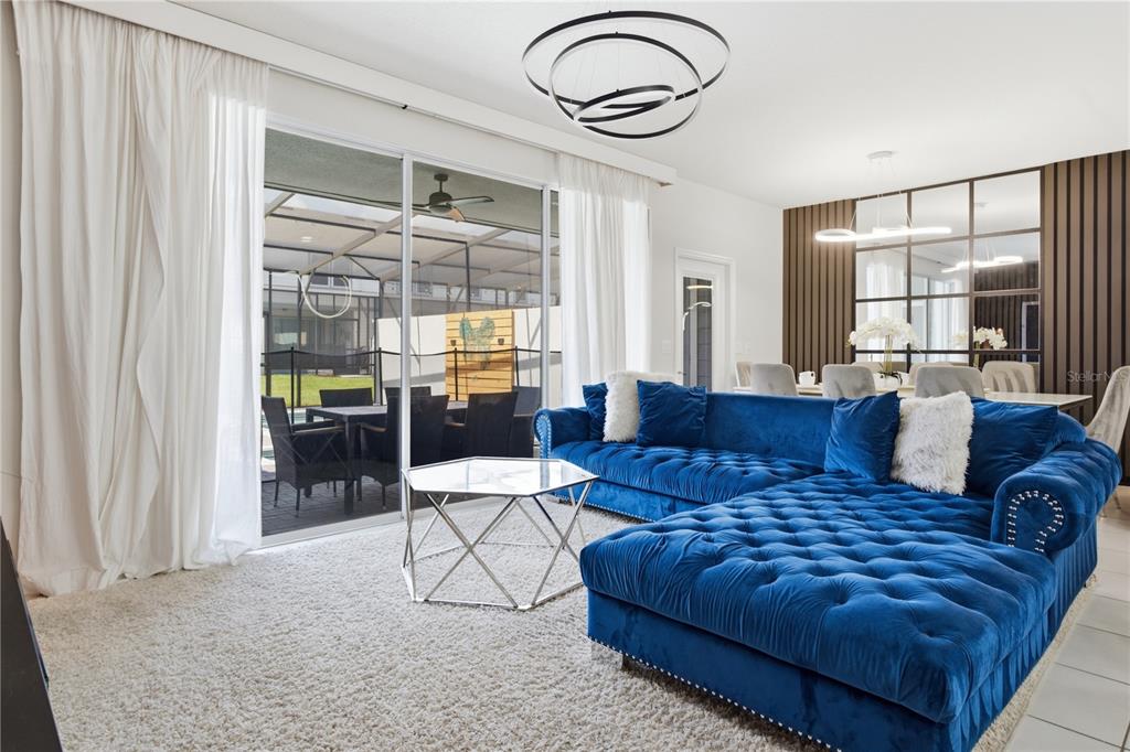 A living room features a blue tufted sectional, a glass coffee table, and a patio view — 3954 LANA AVENUE, DAVENPORT, FL