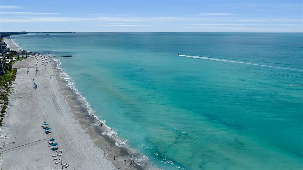 An aerial view shows a sandy beach area with several blue-roofed pavilions and palm trees — 1915 HARBOUR LINKS CIRCLE UNIT 6, LONGBOAT KEY, FL