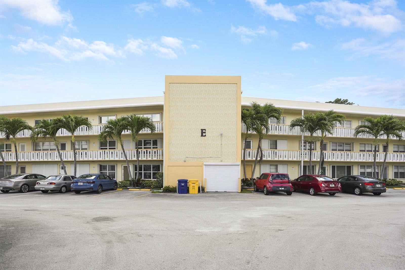 A three-story apartment building with a central yellow facade marked with the letter E — 210 Wellington E, West Palm Beach FL 33417, WEST PALM BEACH, FL